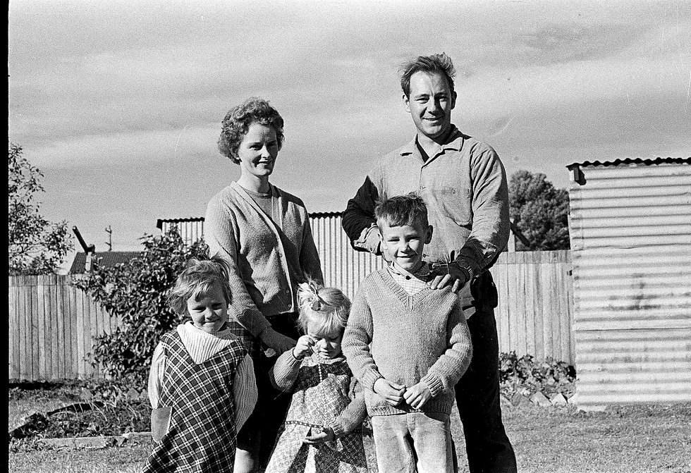 Derek and Pat standing behind their three young children in a suburban backyard, late 1960s
