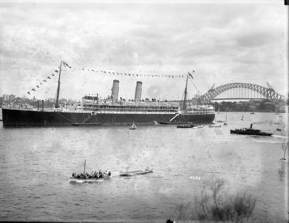 The Orient Line liner RMS Ormonde at anchor in Sydney Harbour, dressed overall, with the partly built Sydney Harbour Bridge behind